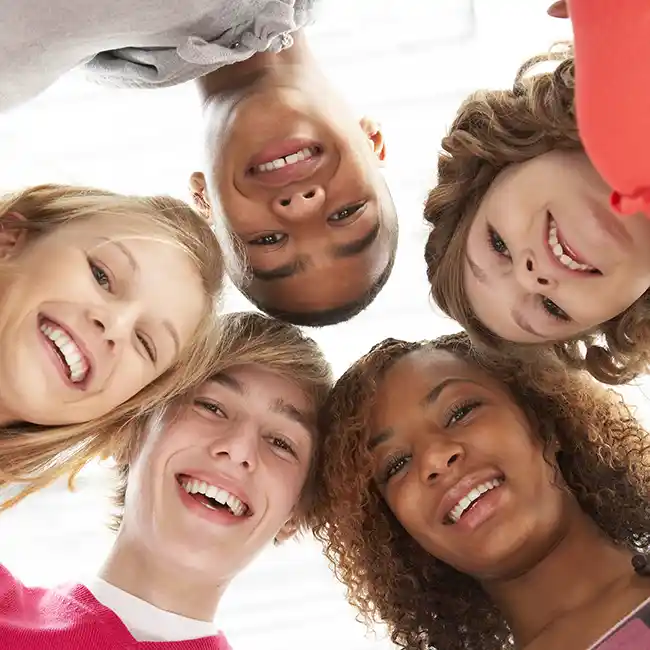 five teenagers in a circle looking down at the camera smiling