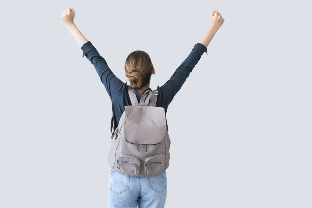 girl with backpack and arms up in the air