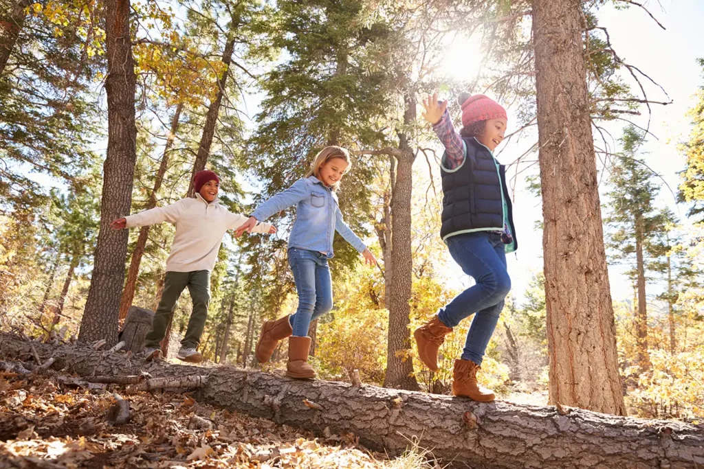 three kids walking on log smiling in forest