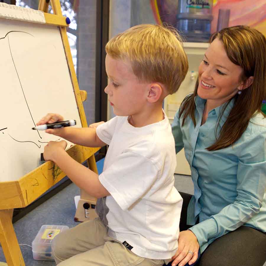 child at easel drawing with occupational therapist assisting